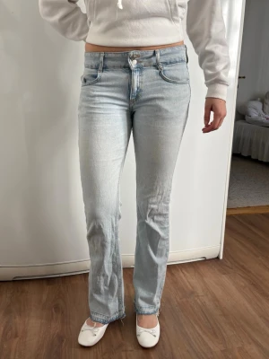Pull & Bear jeans - Snygga ljusblå jeans med raka ben och hög midja. Jeansen har klassiska fem fickor och stängs med dragkedja och två knappar. De är i en mjuk denim med lite stretch för extra komfort. Slitna o förlängda längst ner. Se bilder. Perfekta för en avslappnad och trendig look.