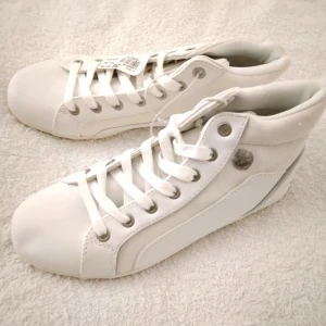 HELT NYA OANVÄNDA Vita höga sneakers, felfria, Storlek 36 - Ett par nya oanvända, vita höga snygga sneakers med tags/prislappen kvar på, i immitationsläder. Populära och slutsålda i butik. Perfekt för en avslappnad och stilren look i vår/sommar. Bekväma och passar till många olika outfits. Storlek 36. Skickas inplastade i originalförpackning. Modellen visar liknande skor.
