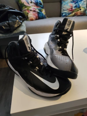 Nike air svart/grå basket sneakers high - Säljer ett par Nike air sneakers i high-modell med svart och grå färg, stora vita swoosh-loggor och svarta skosnören. Skorna har ventilerande meshpartier och robust gummisula, perfekta för basket eller streetstyle.