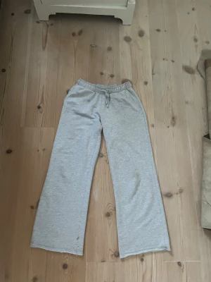 Grå mjukisbyxor  - Ett par ljusgrå lågmidjade loungebyxor i mjukt material med resårmidja och dragsko. Har sprättat upp dom längst ner för att jag vill ha de längre men det synns typ inte alls. Byxorna har raka ben och avslappnad passform, perfekta för chill hemma. Klassisk enkel design utan synliga loggor eller detaljer.