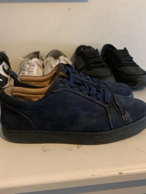 Christian Louboutin mörkblå  - Snygga mörkblå sneakers i mocka med svarta gummisulor och matchande blå skosnören. Lågt skuren modell med klassisk design och diskreta sömmar. Perfekta för en stilren och avslappnad look.