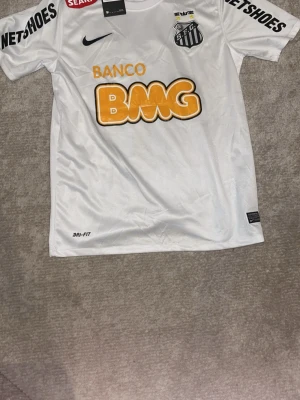 Vit Santos Neymar Jr matchtröja - Säljer en vit Santos FC matchtröja från Nike med Neymar Jr och nummer 11 på ryggen. Tröjan har tryckta sponsorer som BMG och Netshoes, samt klubbmärke på bröstet. Tillverkad i Dri-FIT material som andas, perfekt för fotbollsträning eller match.