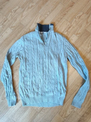 Ljusgrå kabelstickad tröja med halvzip herr stl S - Ljusgrå kabelstickad tröja med halv dragkedja och hög krage.  Perfekt för dig som gillar klassisk och stilren look. Herr stl S