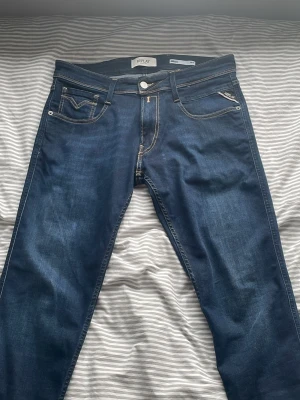 Mörkblå jeans från Replay - Snygga mörkblå jeans från Replay med klassisk femficksmodell och kontrastsömmar. Jeansen har raka ben och detaljerade bakfickor med broderi. Tillverkade i mjukt denimtyg som ger en bekväm passform.