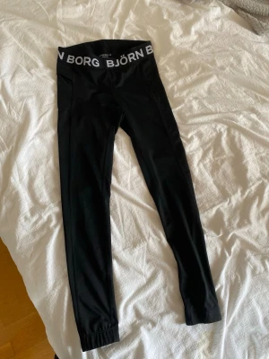 Svarta löpartights från Björn Borg strl 36 - Snygga svarta leggings/löpartights från Björn Borg med bred resår i midjan där loggan står tryckt i vitt. Modellen är åtsittande och tillverkad i stretchigt funktionsmaterial, perfekt för träning eller chill. Modellen heter Hydro-Pro.