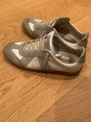 Gråvita sneakers i mocka och läder - Snygga sneakers i grå mocka och vitt läder med klassisk låg profil och neutrala färger. Skorna har vita och grå paneler, beige snörning och en tunn yttersula. Perfekta för en stilren och avslappnad look. Skorna tvättas även innan de postas! Hör gärna av er kring frågor eller prisförslag!