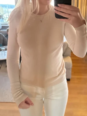 Beige långärmad tröja - Säljer en enkel och stilren beige långärmad tröja i mjukt, tunt material. Tröjan har rund halsringning och en figurnära passform som passar perfekt till jeans eller kjol. Perfekt basplagg för alla tillfällen.