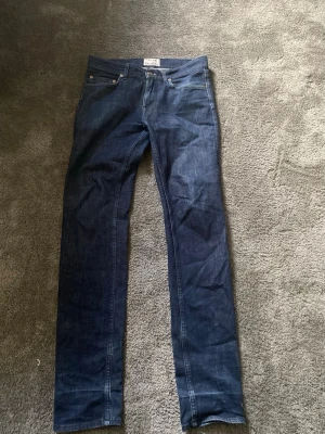 Mörkblå raka jeans från Nudie - Snygga mörkblå jeans från Nudie med klassisk femficksdesign och raka ben. Jeansen har en stilren look och är tillverkade i denim med lätt tvättad finish. Perfekta för dig som gillar en enkel och tidlös stil.