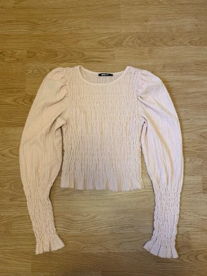 Ljusrosa smockad topp blus med puffärm - Ljusrosa topp från Gina Tricot med smockad struktur och puffiga ärmar. Strl XS