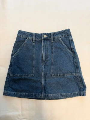 Blå jeanskjol med fickor - Snygg blå jeanskjol i klassisk modell med stora framfickor och bakfickor. Kjolen har bälteshällor och stängs med knapp och dragkedja framtill. Perfekt till vardags för en avslappnad och trendig look 🤍