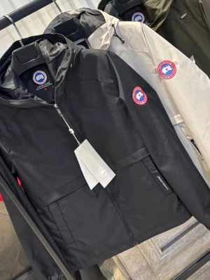 Svart jacka från Canada Goose - Snygg svart jacka från Canada Goose med huva och dragkedja framtill. Jackan har en klassisk passform, logotyp på ärmen och praktiska fickor. Perfekt för dig som vill ha en stilren och funktionell jacka.