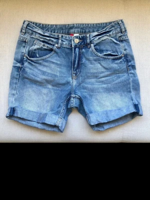 Vintage H&M Divided Denim Shorts – Låg midja – Y2K / 00-tal – Stl 36 - Säljer ett par riktigt snygga jeansshorts från H&M Divided, köpta för ca 20 år sedan. De har den eftertraktade låga midjan (low waist) som är typisk för tidigt 2000-tal och är i fantastiskt vintage-skick! Klassisk 5-ficksmodell i kraftig 100% bomull (ingen stretch) för den rätta looken. Uppvikta benslut och en unik "Love Me Love You"-patch på baksidan. Mått (mätta platt): • Midjebredd: 40 cm (sitter på höften) • Längd: 36 cm • Innerbenslängd: 12 cm Ett unikt fynd med helt rätt patina!