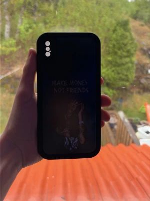 Svart mobilskal med textmotiv - Snyggt svart mobilskal med texten 'MAKE MONEY NOT FRIENDS' och ett tryck av en person. Skalet har tre hål för kameran och är gjort i ett tåligt material som skyddar mobilen. Perfekt för dig som vill ha en cool och personlig look på mobilen.