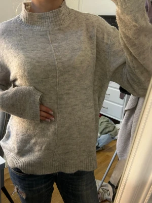 Beige stickad tröja med hög krage - Mysig beige stickad tröja med hög ribbad krage och raka ärmar. 