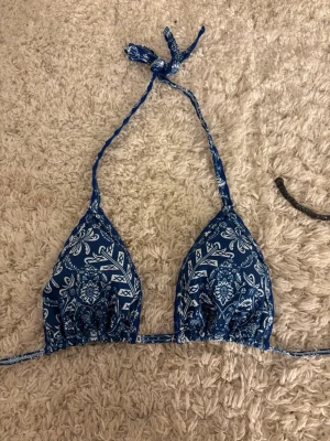 Blå bikiniöverdel med paisleymönster - Snygg blå trekantsbikini med vitt paisleymönster och knyt i nacken och ryggen. Perfekt för stranden eller poolen, ger en trendig och ungdomlig look.