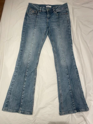 Ljusblå bootcut jeans med brodyr - Säljer ett par ljusblå bootcut jeans med dekorativa sömmar på bakfickan och pressveck framtill. Jeansen har klassisk femficksmodell och är tillverkade i denim med snygg tvätt. Perfekta för en avslappnad men trendig look.