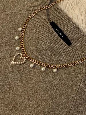Guldfärgat halsband med pärlor och hjärta - Snyggt guldfärgat halsband med kedja, dekorerat med vita pärlor och ett hjärtformat hänge av små pärlor. Perfekt accessoar för att lyfta din outfit med en trendig och söt detalj.