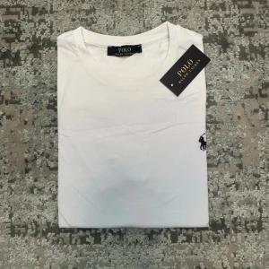 Vit snygg t-shirt - Klassisk vit t-shirt med rund halsringning och korta ärmar. T-shirten har den ikoniska broderade loggan på bröstet och är tillverkad i mjuk bomull för en skön känsla. Perfekt basplagg till garderoben.