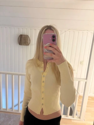 Gul kofta från Gina Tricot - Snygg ljusgul ribbad kofta från Gina Tricot med långa ärmar och knappar framtill. Figurnära passform och mjukt material som känns skönt mot huden. Perfekt att styla med jeans eller kjol för en trendig look.