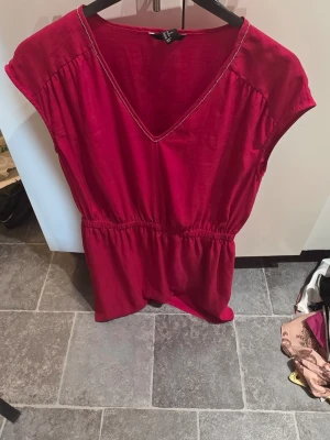 Röd kortärmad klänning H&M - Snygg röd klänning från H&M med v-ringning och resår i midjan. Klänningen har korta ärmar och är tillverkad i ett mjukt, lätt material som känns skönt mot huden. Perfekt för dig som vill ha en enkel men stilren look.
