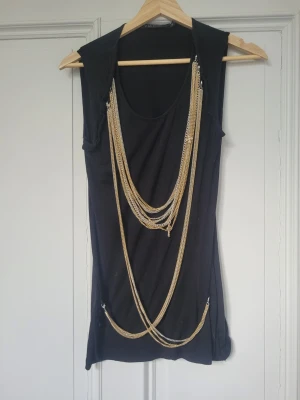 Svart ärmlös topp med kedjedetaljer - Cool svart ärmlös topp från w les femmes med flera kedjor i guld och silver som hänger över framsidan. Kedjorna är fästa i små öglor som gör att man kan flytta rund kedjorna som man vill! Perfekt för dig som vill sticka ut och gillar statement-detaljer. Använd 1 gång!
