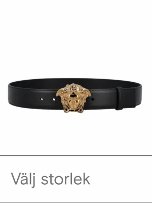 Svart Versace La Medusa bälte - Snyggt svart bälte från Versace med ikoniskt Medusa-spänne i guld. Tillverkat i exklusivt skinn och perfekt för att lyfta vilken outfit som helst. Bältet har klassisk design med justerbara hål och elegant finish.