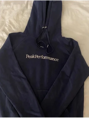 Mörkblå hoodie från Peak Performance - Mörkblå hoodie med vit Peak Performance text på framsidan! I storlek M men skulle säga att den passar en S-XS bättre😊