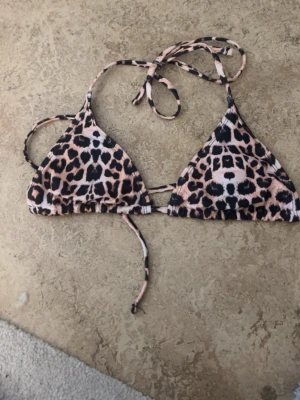 Leopardmönstrad trekantsbikini - Snygg trekantsbikini med leopardmönster i svart och beige. Bikinin har knytband i nacken och ryggen för justerbar passform. Perfekt för sommardagar på stranden eller vid poolen.