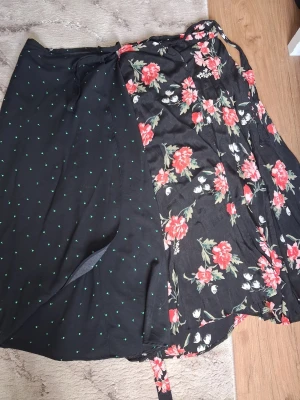 2st Svarta långkjolar med gröna prickar & blommor - Säljer 2st  svart långkjol med små gröna prickar och omlottmodell. Kjolen har knytband i midjan och är tillverkad i ett mjukt och lätt tyg som passar perfekt till varmare dagar. Enkel men ändå unik design som är lätt att matcha. Passar även dig som bär S!