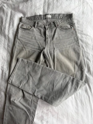 Grå raka jeans  - Säljer ett par grå jeans med rak passform och klassisk design. Jeansen har normal midja och är tillverkade i bomull. Perfekta för en avslappnad och stilren look.