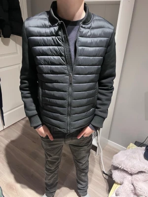 Svart pufferjacka från Colmar - Snygg svart pufferjacka från Colmar med quiltad framsida och släta ärmar. Jackan har ribbade muddar, ståkrage och dragkedja framtill. Märkeslogga på ärmen och två sidofickor. Perfekt för kyliga dagar och enkel att matcha med olika outfits.