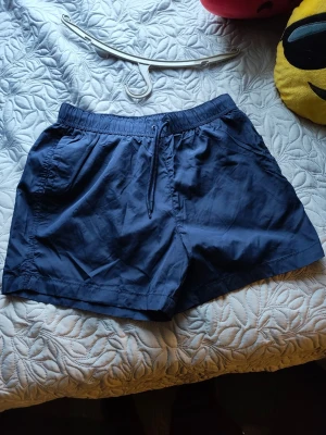 Mörkblå shorts med snörning - Snygga mörkblå shorts med elastisk midja och snörning framtill. Shortsen har sidofickor och är tillverkade i ett lätt och svalt material, perfekta för varma dagar. Passformen är normal och de har en enkel, stilren design.