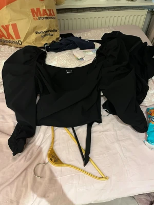 Svart omlottopp med puffärmar - Trendig svart omlottopp från gina tricot med stora puffärmar och knytband i midjan. Toppen har en fyrkantig ringning och är perfekt för dig som vill sticka ut med en cool och modern look. helt ny aldrig använd. 
