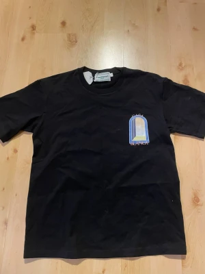 Svart t-shirt från Casablanca - Snygg svart t-shirt från Casablanca med ett färgglatt tryck på bröstet som föreställer en båge och texten 'Casa Blanca'. Klassisk passform och rund halsringning. Perfekt till jeans eller shorts.