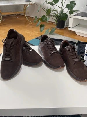 Bruna sneakers i mocka och läder - Snygga bruna sneakers med ovandel i mocka och detaljer i läder. Skorna har bruna snören, robust sula med mönster för extra grepp och en stilren design som passar till många outfits. Perfekta för dig som gillar en klassisk men modern look.helt ny,fick i present men storlek passa inte. En av skorna är 44 och den andra 42. Ny pris 1300 för en men jag säljer båda för 1300.så en för 650