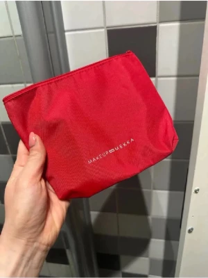 Röd necessär från Makeup Mekka - Snygg röd necessär från Makeup Mekka i slitstarkt tygmaterial. Perfekt för att förvara smink, penslar eller småprylar. Stängs med dragkedja och har en enkel, stilren design med logga på framsidan.