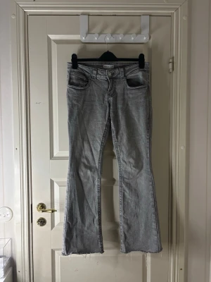 Grå bootcut jeans från Gina Tricot - Säljer ett par ljusgrå bootcut jeans från Gina Tricot. Jeansen har klassisk femficksmodell, hög midja och råa, avklippta benslut för en trendig look. Perfekta för dig som är kurvig och kortare i längden (jag är 155cm)