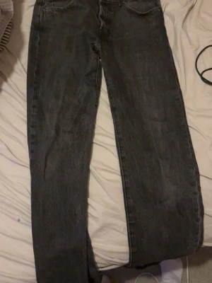 Svartgråa raka jeans med fem fickor - Säljer ett par svartgråa jeans med rak passform och klassisk femficksdesign. Jeansen har normal midja och är tillverkade i ett slitstarkt denimtyg. Passar perfekt till en avslappnad stil och är lätta att matcha med olika plagg.
