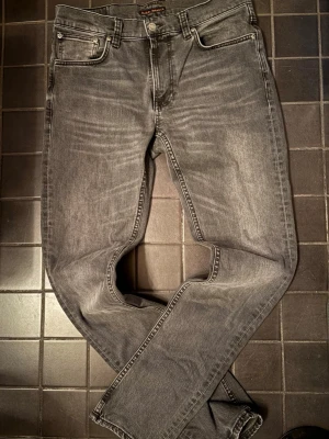 Grå jeans från Nudie Jeans - Säljer ett par gråa jeans i modellen Grim Tim från Nudie Jeans med storleken 32/34. Jeansen har en snygg tvättad look och raka ben. Perfekta för dig som gillar stilrena och tidlösa jeans i mjukt denimtyg. 9/10 skick, lätt använda