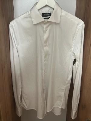 Klassisk vit skjorta från Dressmann - Säljer en stilren vit skjorta från Dressmann med klassisk krage och dolda knappar framtill. Skjortan har lång ärm och är gjord i ett mjukt bomullstyg som känns skönt mot huden. Perfekt till alla tillfällen där du vill vara lite extra uppklädd. Sjortan är använd 3 gånger 