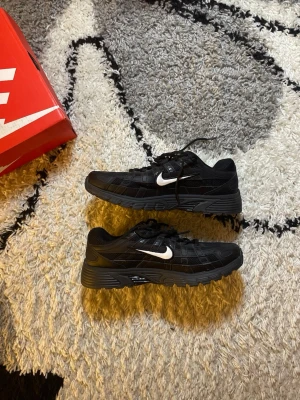 Nike p6000 Svart vit - Snygga svarta Nike sneakers med vit swoosh på sidan. Skorna har en chunky sula och är tillverkade i mesh och syntetmaterial för en sportig look. Perfekta för dig som gillar streetwear och vill ha bekväma skor med stilren design.