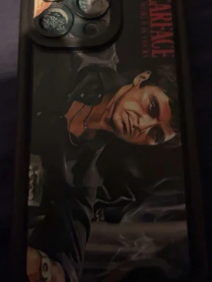 Scarface mobilskal med motiv - Snyggt mobilskal med Scarface-tema och färgstarkt motiv av Tony Montana. Skalet är svart runt kanterna och har en tryckt bild på baksidan med texten 'Scarface'. Passar dig som gillar filmklassiker och vill ha ett unikt skal till mobilen.