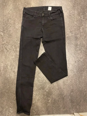 Svarta skinny jeans från H&M - Säljer ett par svarta skinny jeans från H&M med låg midja. Jeansen är i stretchigt denimtyg och har klassisk femficksmodell. Perfekta för dig som gillar en tight passform och enkel stil.