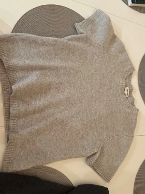 Grå stickad tröja Soft Goat - Mysig grå stickad tröja från Soft Goat i storlek S. Tröjan har korta ärmar, rund halsringning och ribbade kanter vid ärmslut och nederkant.