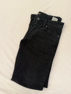 Svarta slim fit jeans från Jack and Jones  - Snygga svarta slim fit jeans från Jack and Jones med klassisk femficksdesign och knappgylf. Jeansen har en lätt tvättad look och är tillverkade i mjukt denimtyg som sitter skönt. Perfekta för en stilren och avslappnad outfit.