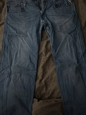 Blå jeans från replay - Säljer ett par klassiska blå jeans från replay anbass med raka ben och fem fickor. Jeansen har snygga detaljer på bakfickorna och är gjorda i mjuk denim. Perfekta för en avslappnad och stilren look. W33 l 30