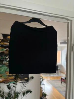 Svart kortkjol från Åhléns - En stilren svart kortkjol från Åhléns i storlek M (40/42). Kjolen har en enkel, rak passform och är tillverkad i ett mjukt material som känns bekvämt mot huden. Perfekt att matcha med en snygg topp eller stickad tröja.