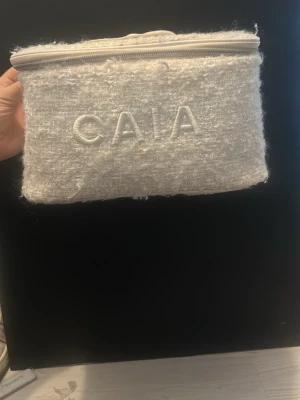 Vit necessär från CAIA i bouclétyg - Säljer en fluffig vit necessär från CAIA med dragkedja och broderad logga på framsidan. Tillverkad i mjukt boucléliknande tyg och har en rektangulär form. Perfekt för smink eller småprylar när du är på språng.