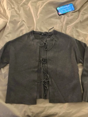 Grå kofta med knytning framtill - Säljer en stilren grå kofta med unika knytband framtill istället för knappar. Koftan har rund halsringning och långa ärmar. Perfekt för dig som gillar minimalistisk och trendig design.