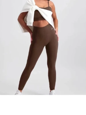 Bruna ribbade leggings Aim'n - Säljer ett par bruna leggings från Aim'n med hög midja och ribbad struktur. De är stretchiga och sitter tight, perfekta för både träning och chill. Metallogo på höften ger en snygg detalj. Materialet är mjukt och följsamt.